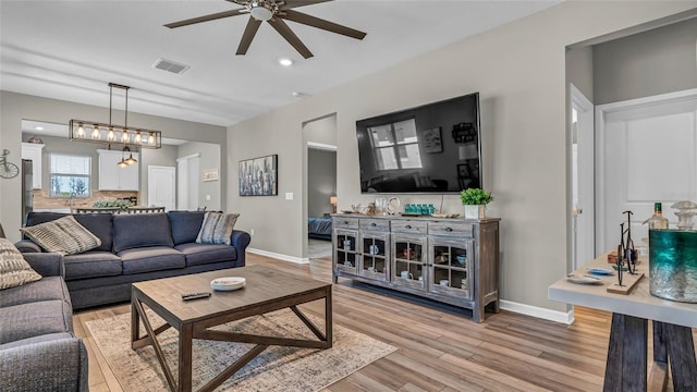 living room featuring light wood finished floors, visible vents, baseboards, and ceiling fan