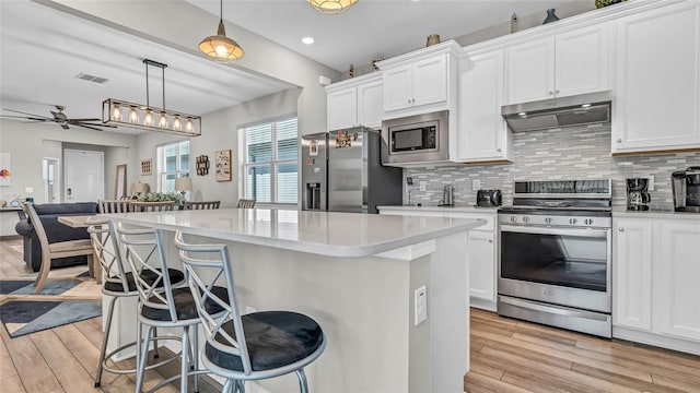 kitchen with a breakfast bar area, ceiling fan, under cabinet range hood, appliances with stainless steel finishes, and tasteful backsplash