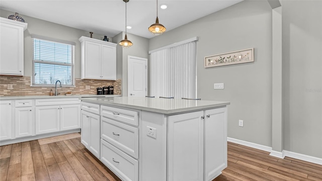 kitchen featuring backsplash, a center island, light countertops, light wood-style flooring, and a sink