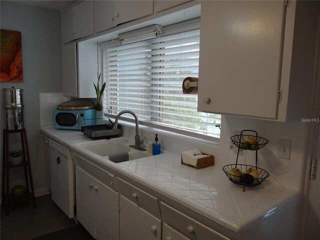 kitchen featuring tile counters, white cabinets, white dishwasher, and a sink