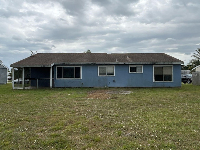 rear view of house featuring a lawn and roof with shingles