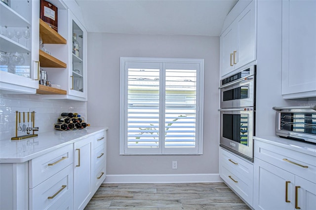 kitchen with stainless steel double oven, open shelves, decorative backsplash, light countertops, and white cabinetry