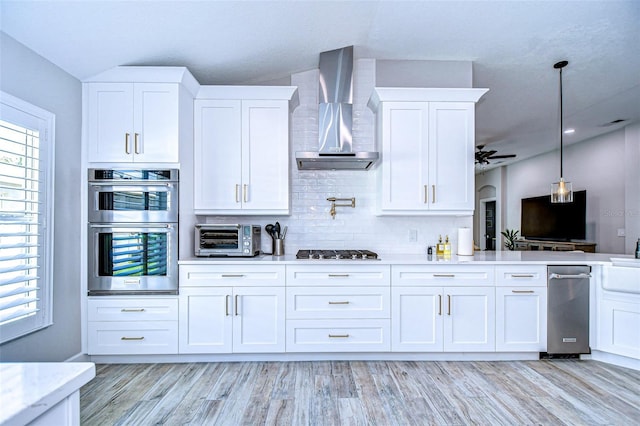 kitchen featuring a toaster, white cabinets, double oven, wall chimney exhaust hood, and backsplash