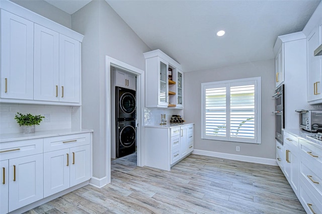 kitchen with white cabinets, light wood finished floors, stacked washer / dryer, decorative backsplash, and baseboards