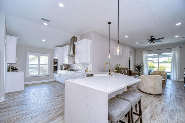 kitchen featuring visible vents, a sink, white cabinetry, wall chimney exhaust hood, and tasteful backsplash