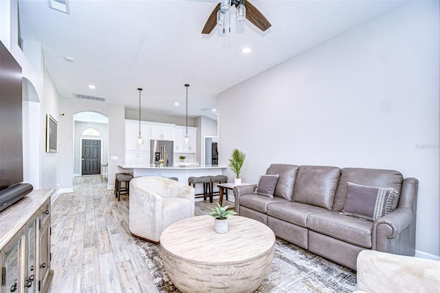 living area featuring a ceiling fan, baseboards, visible vents, arched walkways, and light wood-type flooring