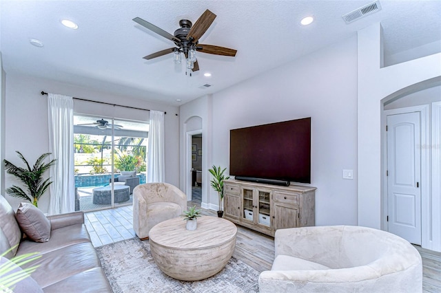 living room with light wood-style flooring, visible vents, arched walkways, and ceiling fan