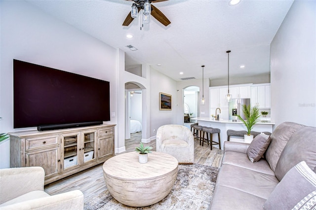 living room with visible vents, light wood-style flooring, recessed lighting, arched walkways, and a ceiling fan