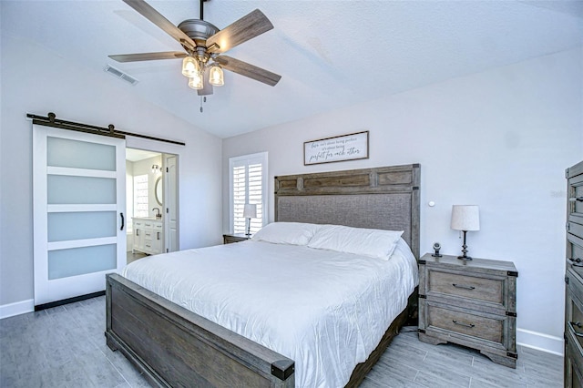 bedroom featuring visible vents, baseboards, a barn door, light wood-style floors, and lofted ceiling