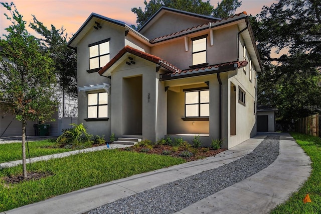 view of front facade featuring a tiled roof, a yard, a garage, and stucco siding