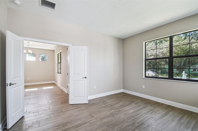 unfurnished room featuring a notable chandelier, visible vents, baseboards, and wood finished floors