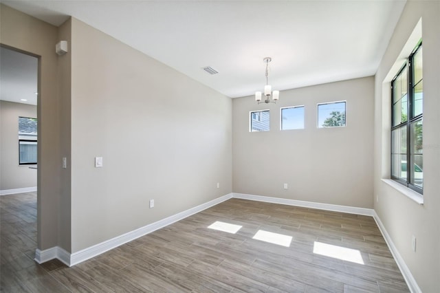 unfurnished dining area featuring visible vents, wood finished floors, baseboards, and a chandelier