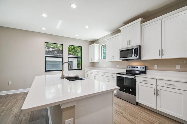 kitchen with wood finish floors, a center island with sink, a sink, appliances with stainless steel finishes, and white cabinets