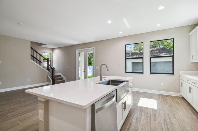 kitchen featuring baseboards, dishwasher, an island with sink, light countertops, and a sink