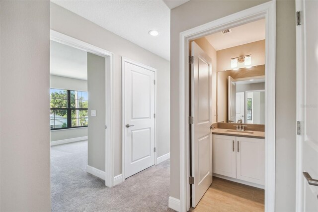 hallway with light carpet, visible vents, baseboards, and a sink