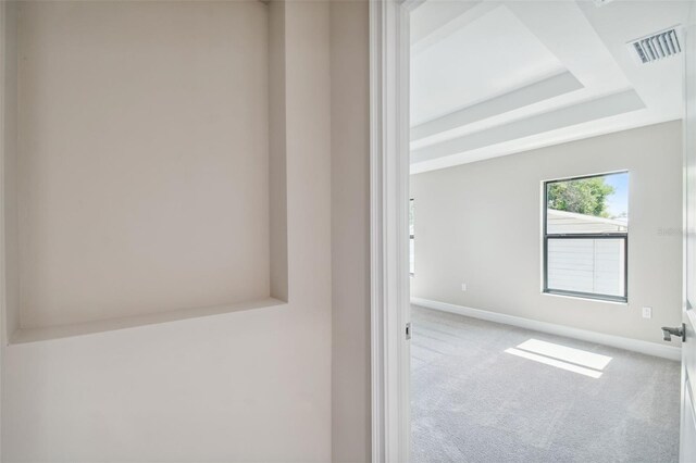 carpeted empty room with visible vents, a raised ceiling, and baseboards