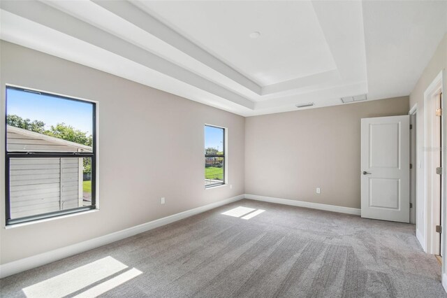 carpeted spare room featuring a tray ceiling, baseboards, and visible vents