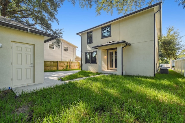 rear view of house with stucco siding, central AC unit, and fence