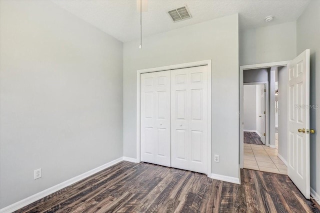 unfurnished bedroom with wood finished floors, visible vents, baseboards, a closet, and a textured ceiling