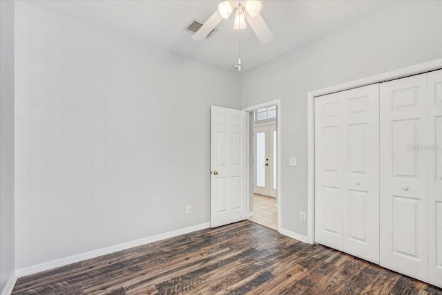 unfurnished bedroom featuring visible vents, baseboards, dark wood-type flooring, and a closet