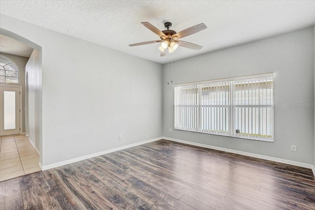 empty room with arched walkways, a textured ceiling, ceiling fan, and wood finished floors