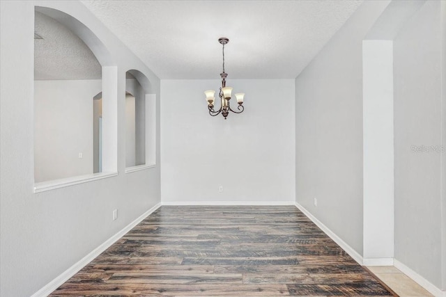 empty room featuring a notable chandelier, wood finished floors, baseboards, and a textured ceiling