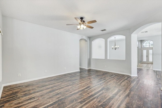 unfurnished room featuring visible vents, arched walkways, dark wood-type flooring, and ceiling fan with notable chandelier