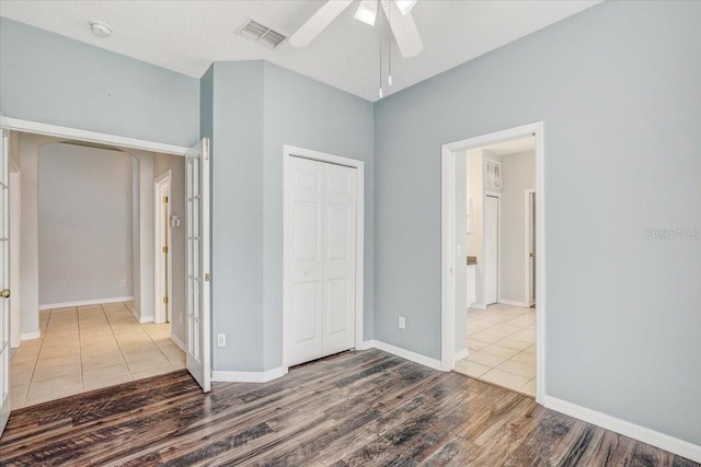 unfurnished bedroom featuring wood finished floors, visible vents, baseboards, ceiling fan, and a closet