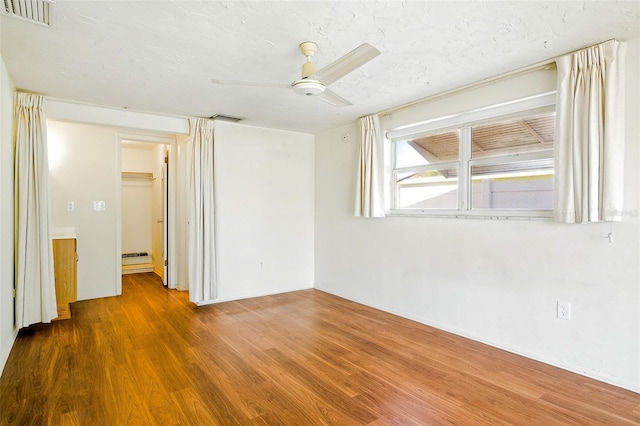 empty room featuring visible vents, a textured ceiling, ceiling fan, and wood finished floors