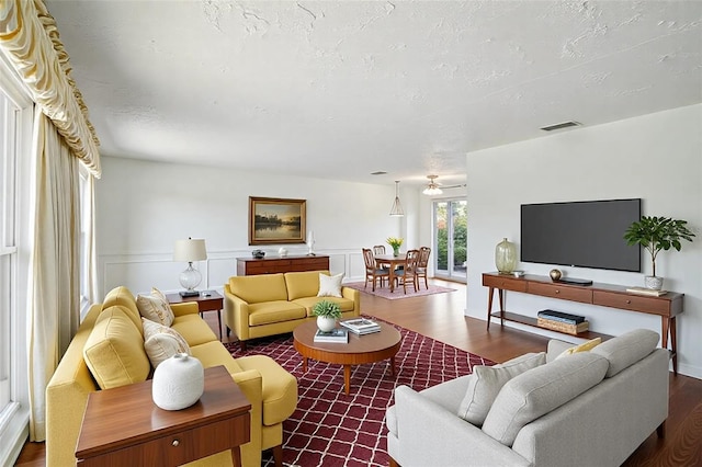 living area with visible vents, a wainscoted wall, wood finished floors, a decorative wall, and a textured ceiling