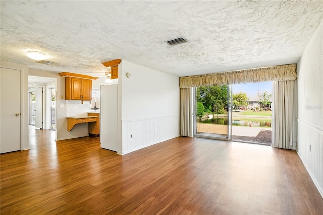 unfurnished living room with a wainscoted wall, wood finished floors, visible vents, and a textured ceiling