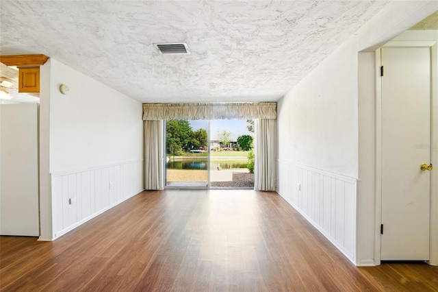 unfurnished room with a wainscoted wall, wood finished floors, and visible vents