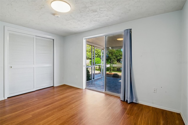 unfurnished bedroom with a closet, wood finished floors, baseboards, and access to exterior