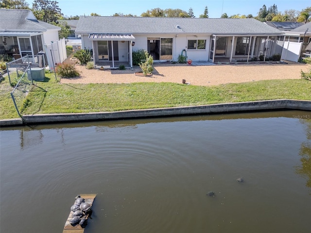 rear view of property with fence, a lawn, a water view, and a sunroom