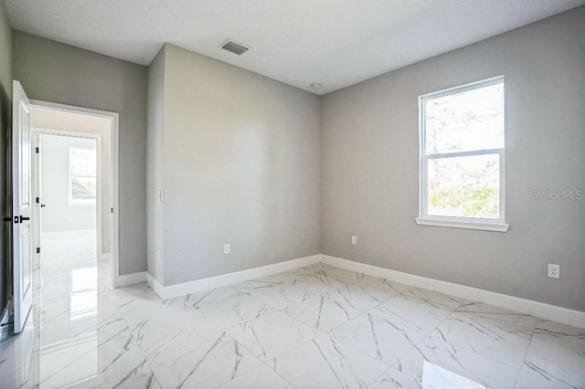 empty room with visible vents, baseboards, a textured ceiling, and marble finish floor