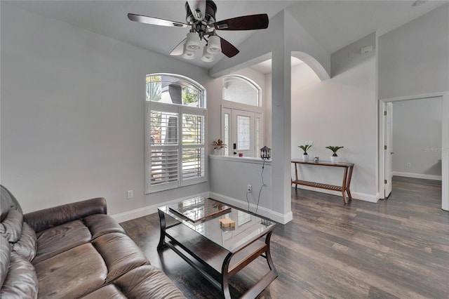 living room with a ceiling fan, dark wood-style floors, arched walkways, a high ceiling, and baseboards