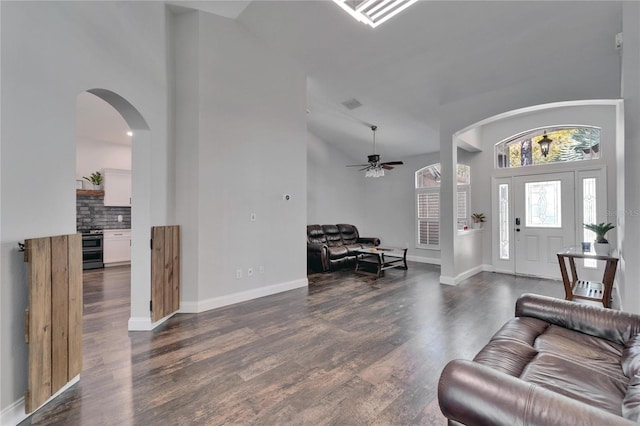 living room with baseboards, arched walkways, ceiling fan, dark wood-type flooring, and a towering ceiling