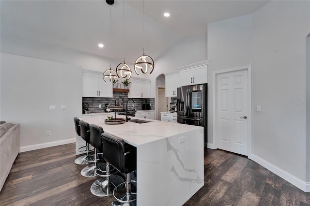 kitchen with backsplash, dark wood-type flooring, refrigerator with ice dispenser, arched walkways, and a sink