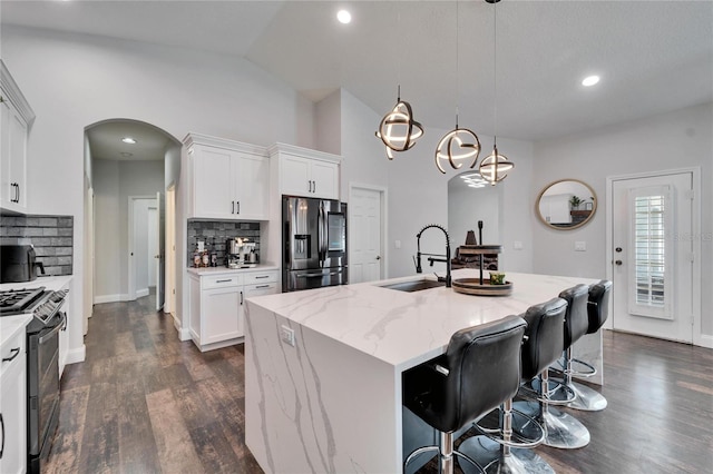 kitchen with dark wood finished floors, arched walkways, a sink, black range with gas cooktop, and stainless steel fridge