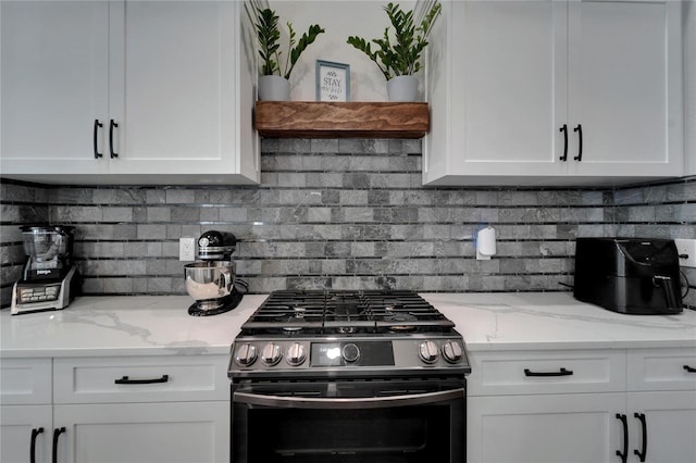 kitchen featuring decorative backsplash, light stone countertops, stainless steel range with gas stovetop, and white cabinetry