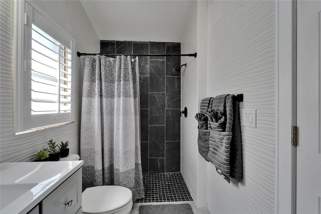 bathroom with a tile shower, toilet, and vanity