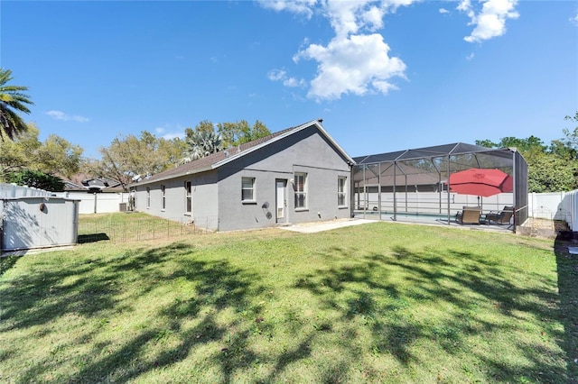 rear view of house featuring a lanai, stucco siding, a lawn, and a fenced backyard