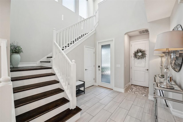 foyer entrance featuring visible vents, baseboards, a healthy amount of sunlight, and a towering ceiling