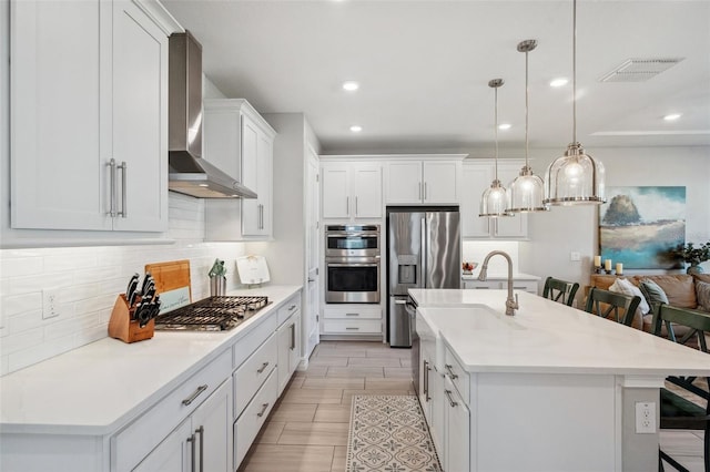 kitchen featuring visible vents, decorative backsplash, appliances with stainless steel finishes, a kitchen bar, and wall chimney range hood