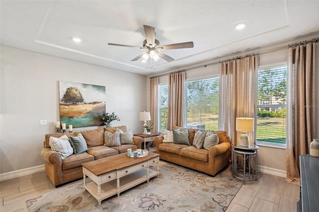 living area with baseboards, a raised ceiling, a healthy amount of sunlight, and light wood finished floors