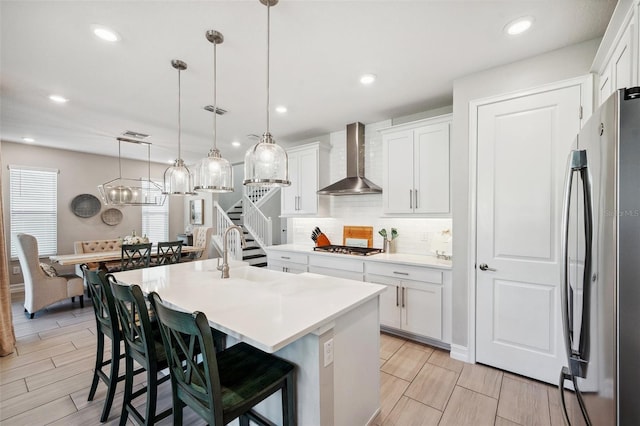 kitchen with a center island with sink, a sink, stainless steel appliances, wall chimney exhaust hood, and decorative backsplash