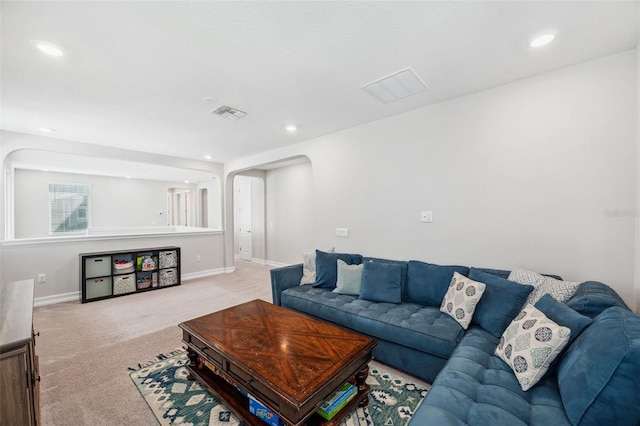 living area featuring baseboards, visible vents, arched walkways, and light carpet