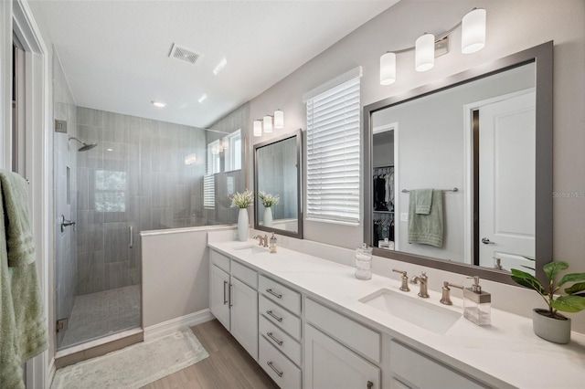 full bath featuring double vanity, wood finished floors, a tile shower, and a sink