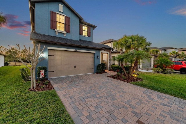 traditional-style home featuring a yard, stucco siding, decorative driveway, and a garage