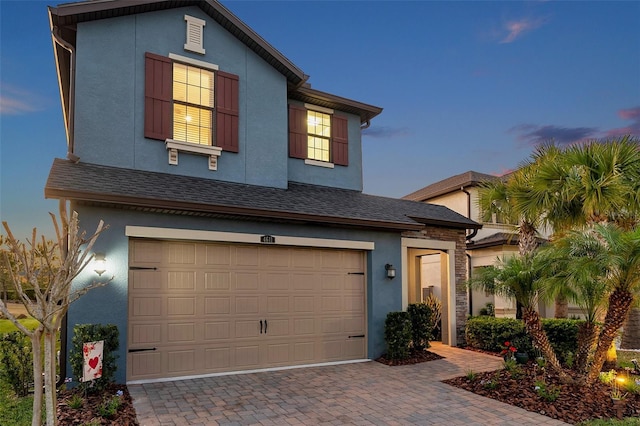 traditional-style home with stucco siding, decorative driveway, and a garage